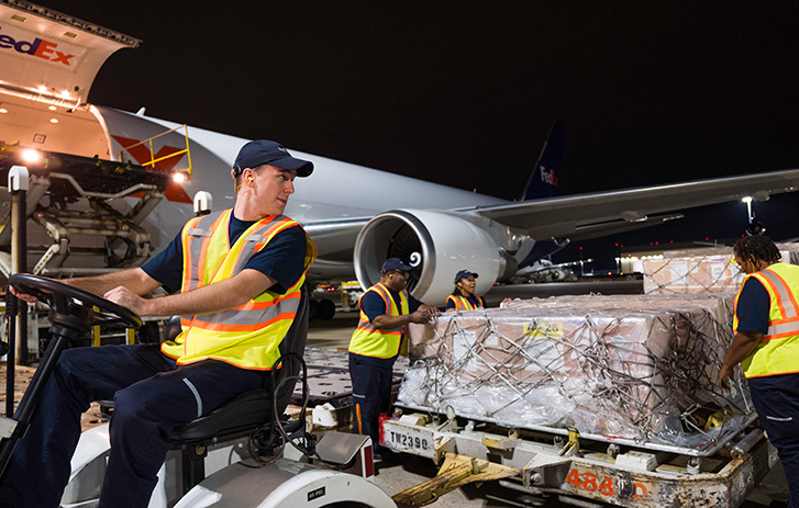 FedEx worker driving a pallet cart beside a FedEx plane