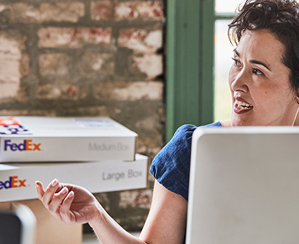 Person at desk reaching past a Medium and Large FedEx box on another desk