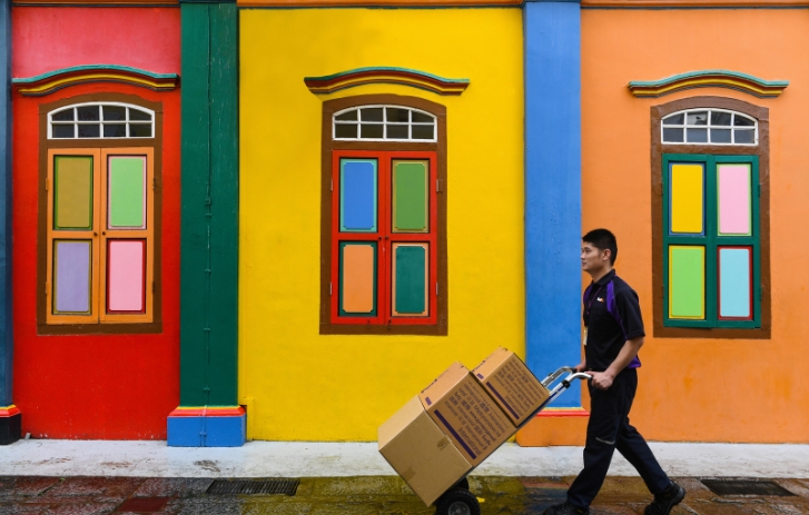 Curier FedEx cu cutii pe un cărucior, în fața unei clădiri colorate