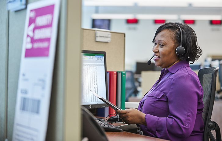 Womanwith headset on smiling and looking at a computer