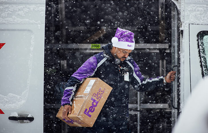Dipendente FedEx che scende dal furgone tra la neve portando un collo