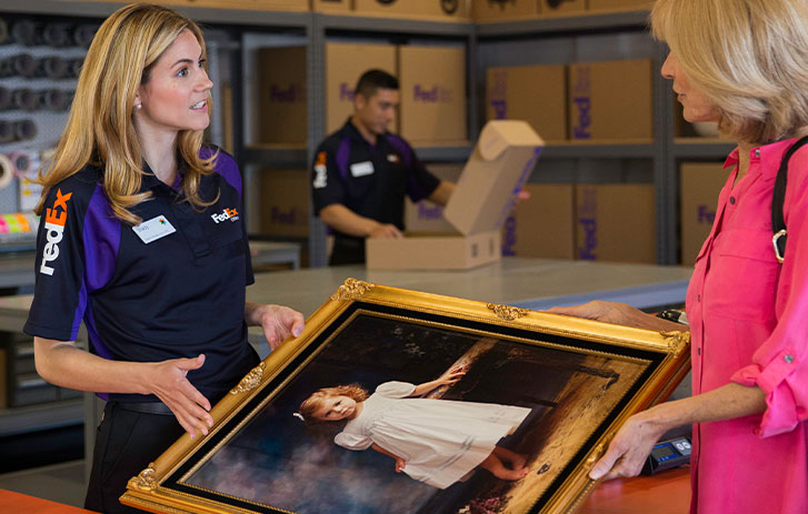 Image of a FedEx Office team member handing over a framed painting to a FedEx Office team member to be packed and shipped.