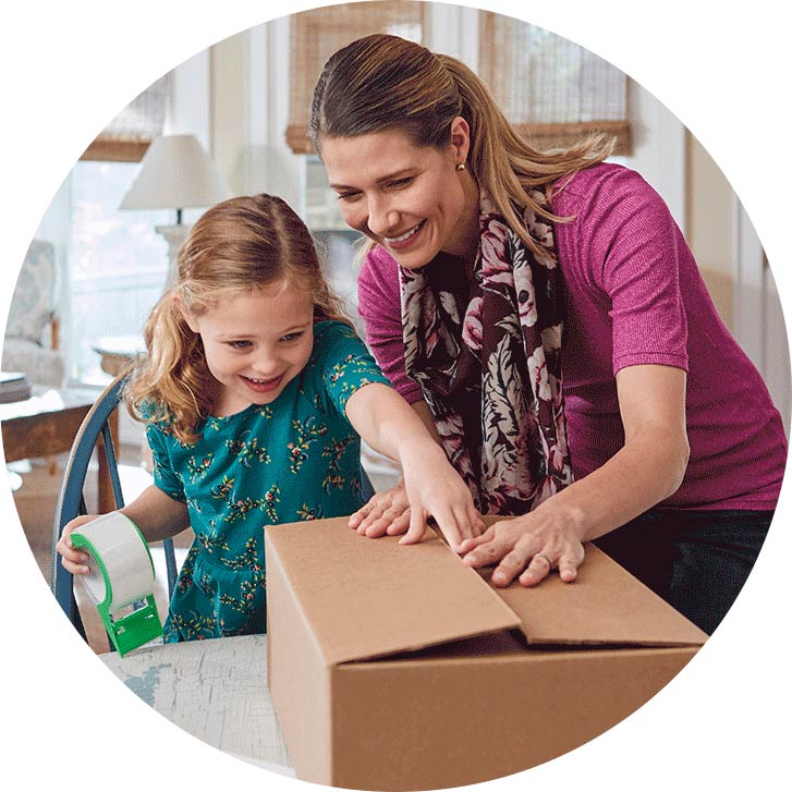 A smiling young girl helps her mom tape a box shut