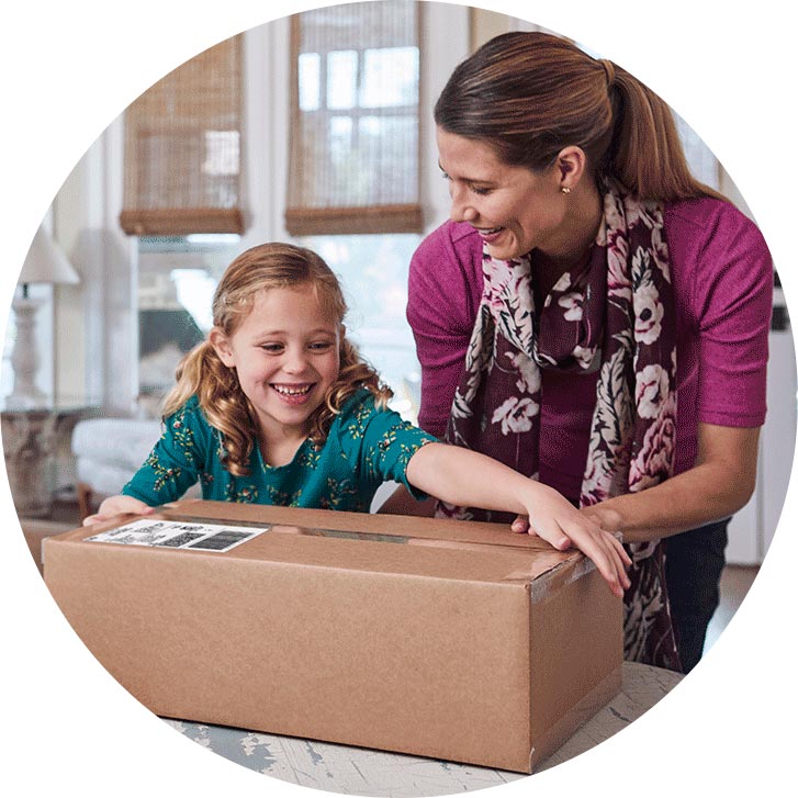 A smiling young girl helps her mom place a shipping label on a box