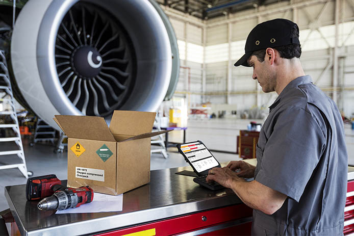 Man types on tablet in warehouse with airplane jet