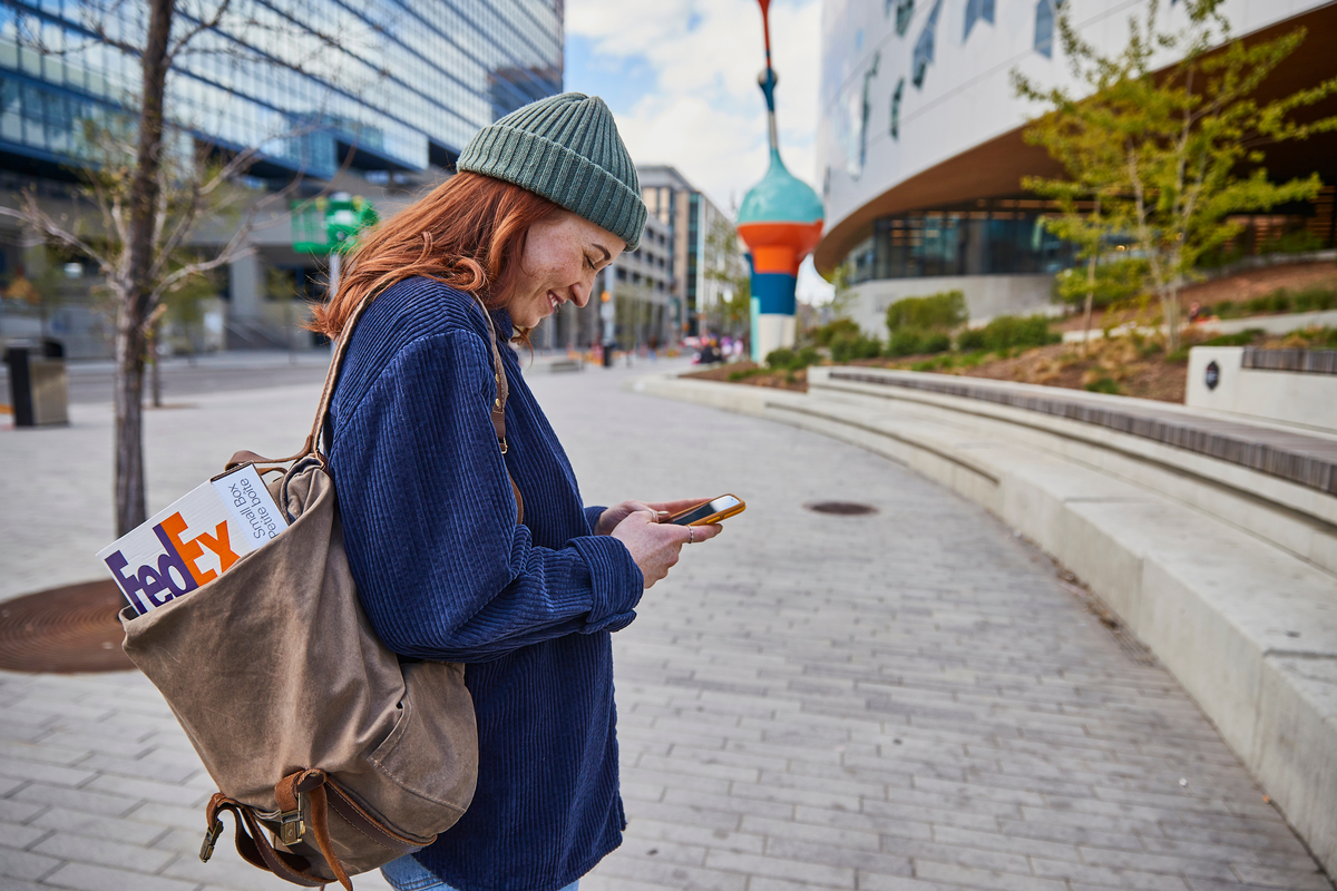 A woman looking at her phone with a FedEx package in her bag.