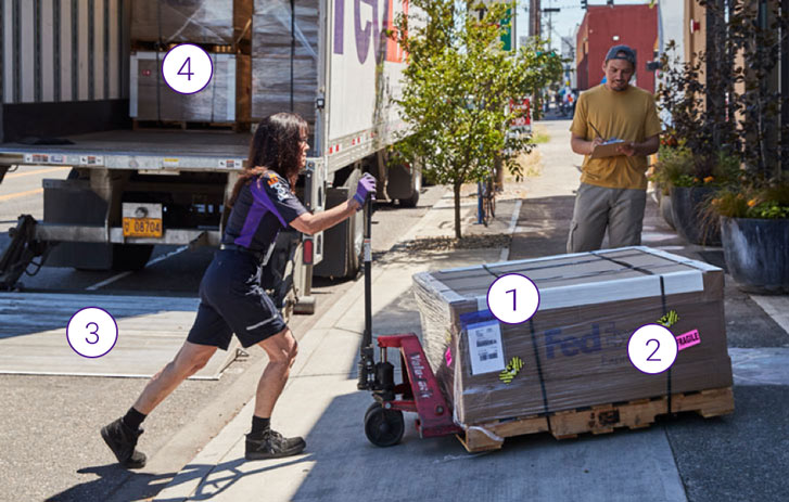 A FedEx Freight employee with freight dolly and shipment a man in background