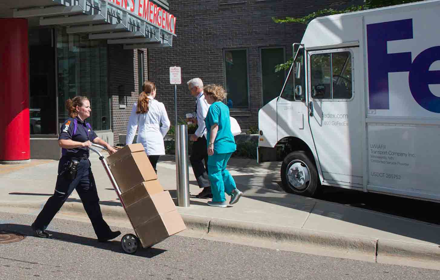 FedEx delivery person walking boxes out of a hospital on a dolley.