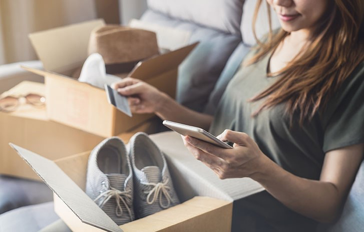 A woman with phone packaging up online return package of shoes