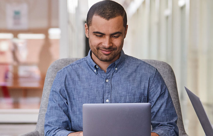 man in blue shirt sitting at desk on computer