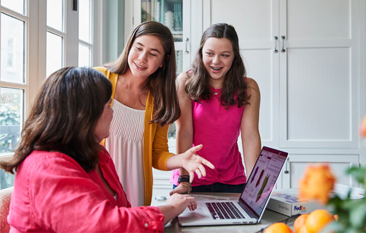 Woman on laptop online shopping and talking with two daughters