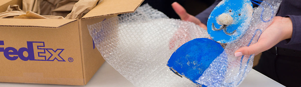 Image of a hand made blue cat item being wrapped in bubble wrap to be packed into a brown FedEx box.