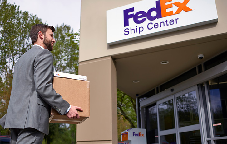 Man in suit carrying boxes into FedEx Ship Center location